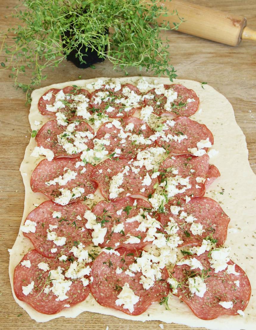 3. Lägg ut hälften av salamiskivorna, oregano och smulad mozzarella på varje degplatta.