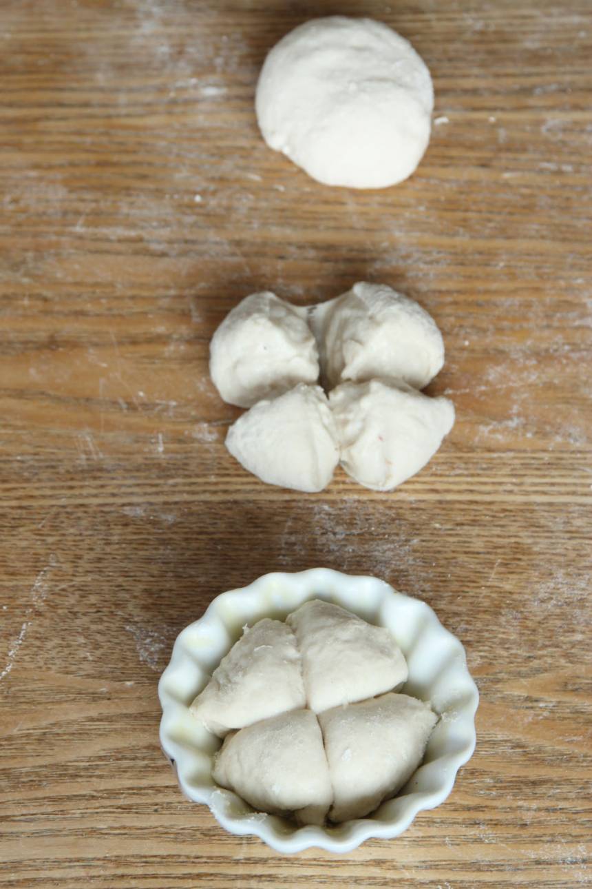 2. Dela degen i 30–34 bitar. Forma runda bullar och skär ett kryss i dem. Lägg dem i muffinsformar av porslin (behöver smörjas) eller papper (behöver inte smörjas). Ställ formarna på en ugnsplåt. Det går också bra att lägga bullarna direkt på en plåt med bakplåtspapper. Låt bröden jäsa under bakduk i ca 30 min. Sätt ugnen på 250 grader. 