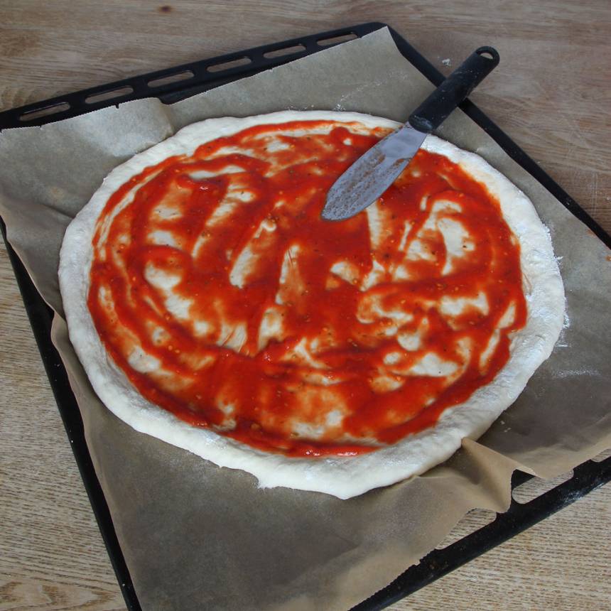 3. Lägg bakplåtspappret med degen på en ugnsplåt. Bred ut pizzasåsen på degen. 