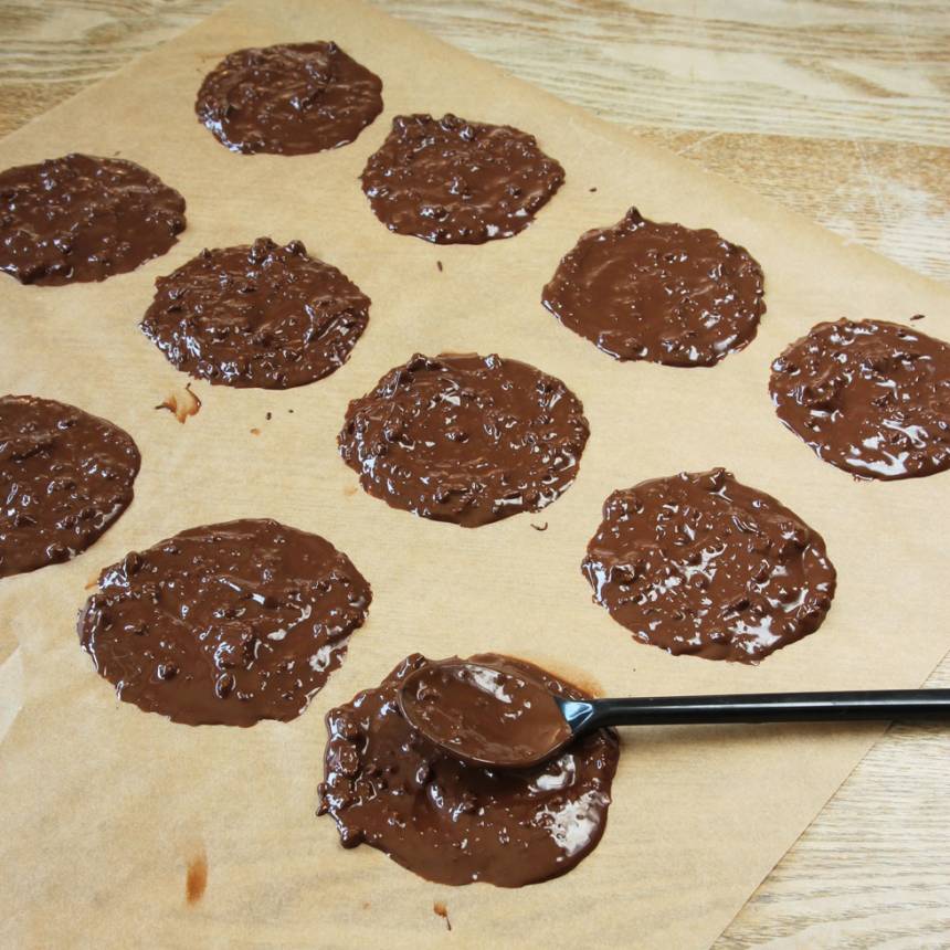 4. Lägg ett bakplåtspapper på en plåt eller skärbräda. Klicka ut chokladen med en matsked och bred ut den till runda plattor. Strö över lite krokant. Låt chokladen stelna i kylen. 